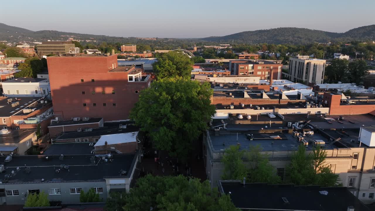 Aerial flight between old historic buildings of small american town at sunrise.Green trees along straight avenue in autumn. Charlottesville City,VA,USA. Wide shot. Paramount Theater along main street.