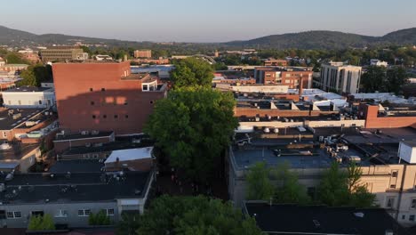 aerial flight between old historic buildings of small american town at sunrise.green trees along straight avenue in autumn. charlottesville city,va,usa. wide shot. paramount theater along main street.