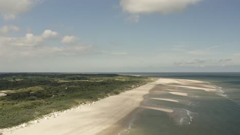 aerial shot flying high over a beautiful white beach and green dunes in oranjezon nature reserve in zeeland, the netherlands