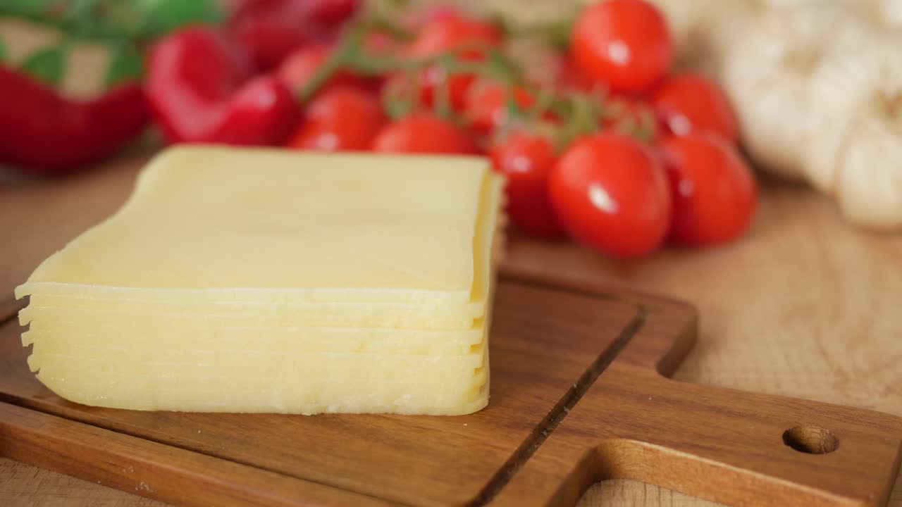 cerca de un bloque de queso en una tabla de corte de madera, con pimientos rojos y tomates cereza en el fondo
