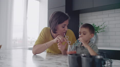 Madre-Joven-E-Hijo-Bebiendo-Jugo-Con-Dulces-En-La-Cocina.-Madre-Feliz-Pasando-Tiempo-Con-Su-Hijo-Sentado-En-La-Mesa-En-Cámara-Lenta