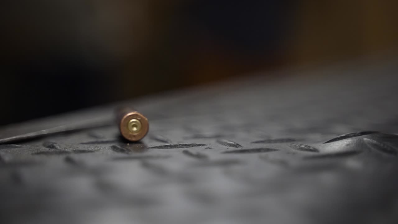 Closeup clip of a bullet shell falling in slow motion onto a black textured surface bouncing and rolling and eventually coming to a standstill