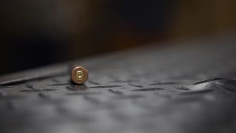 closeup clip of a bullet shell falling in slow motion onto a black textured surface bouncing and rolling and eventually coming to a standstill