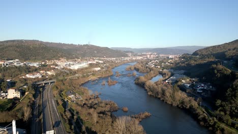 Río-Con-Gran-Vegetación-Y-Construcciones,-Horizonte-Con-Montañas-Y-Cielo-Azul