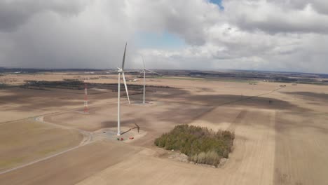 altas turbinas eólicas se elevan sobre campos agrícolas marrones con nubes de tormenta y lluvia en la distancia