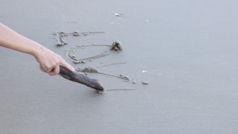 Sequential frames of \"Love\"" being written on sand."