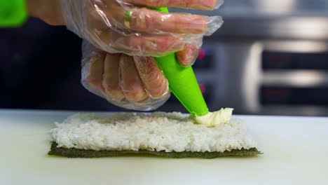 chef in restaurant prepares sushi rolls with tasty ingredients. cook`s hands putting cream cheese. delicious asian food concept.