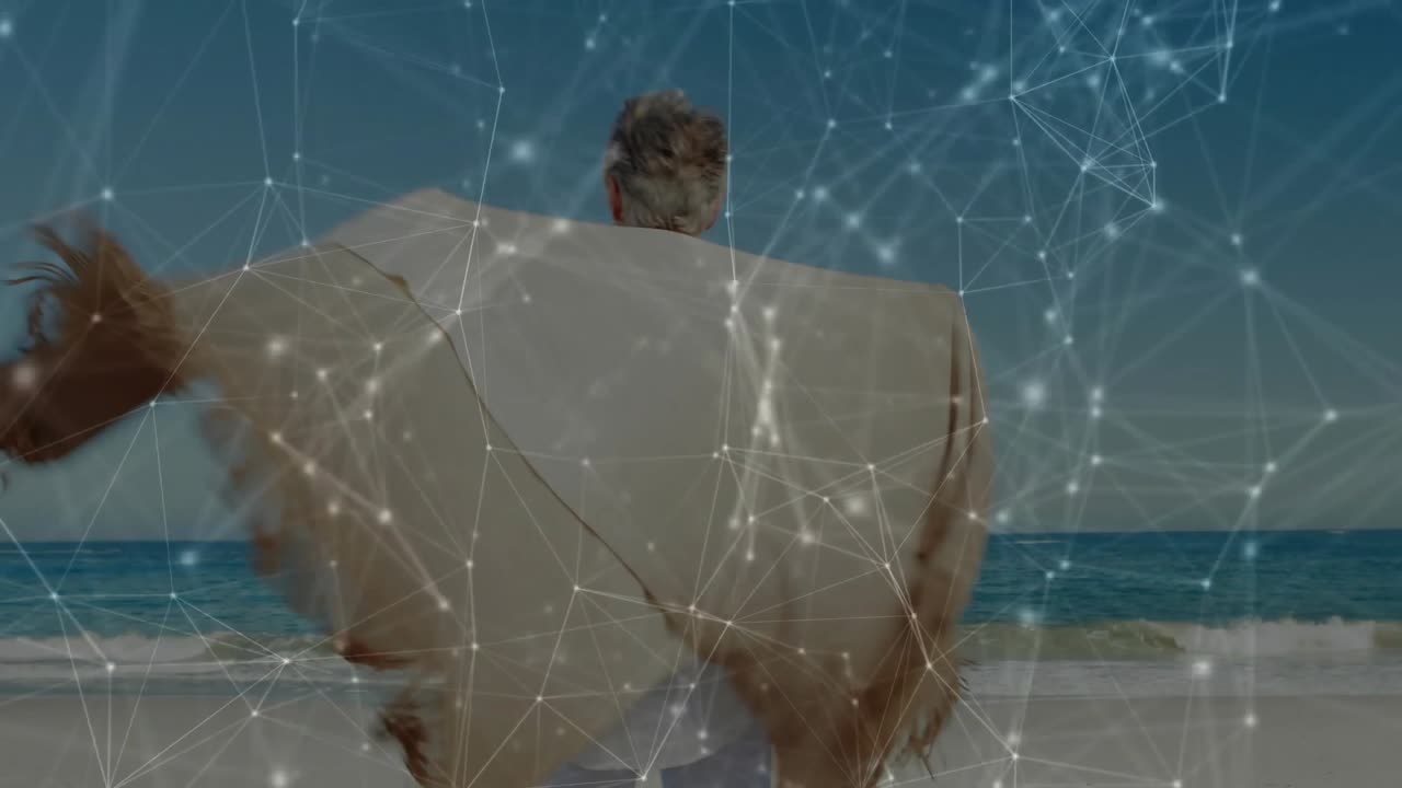 Senior woman holding folded shawl and wrapping it on sandy beach, revealing digital network overlay