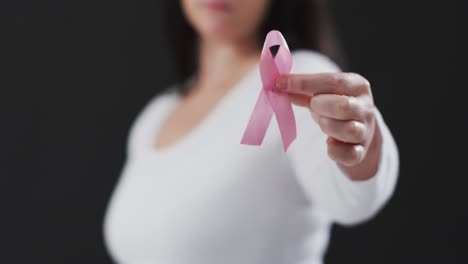 Mid-section-of-woman-holding-a-pink-ribbon-against-black-background