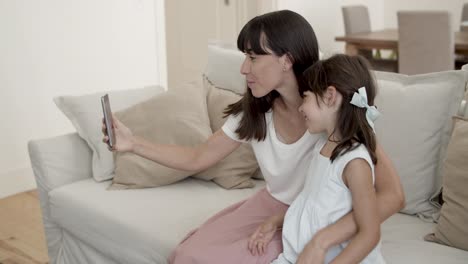 cheerful mom and little daughter holding smartphone