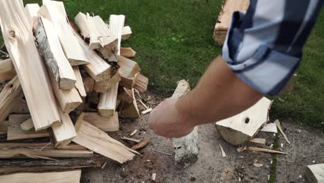 Young man is chopping wood in smaller pieces and putting it aside