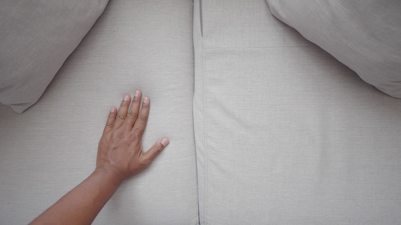 Top-down view of a hand on a beige couch with cushions