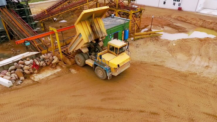 Dump truck dumping sand to conveyor. Sand sorting process on mining conveyor