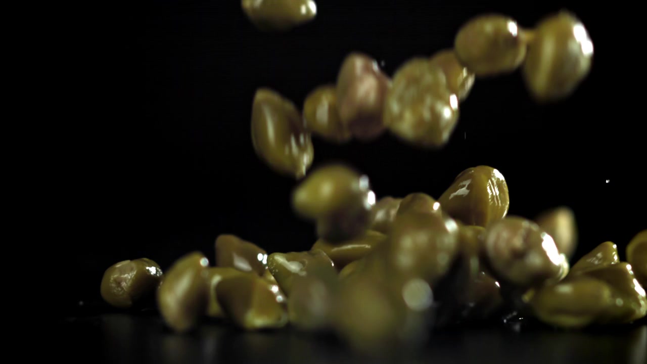 Capperi verdi che cadono e rimbalzano su una superficie nera in movimento rallentato