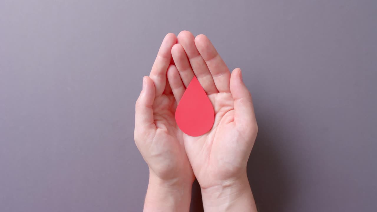 las manos de una mujer caucásica tomando gotas de sangre en un fondo gris, en cámara lenta.