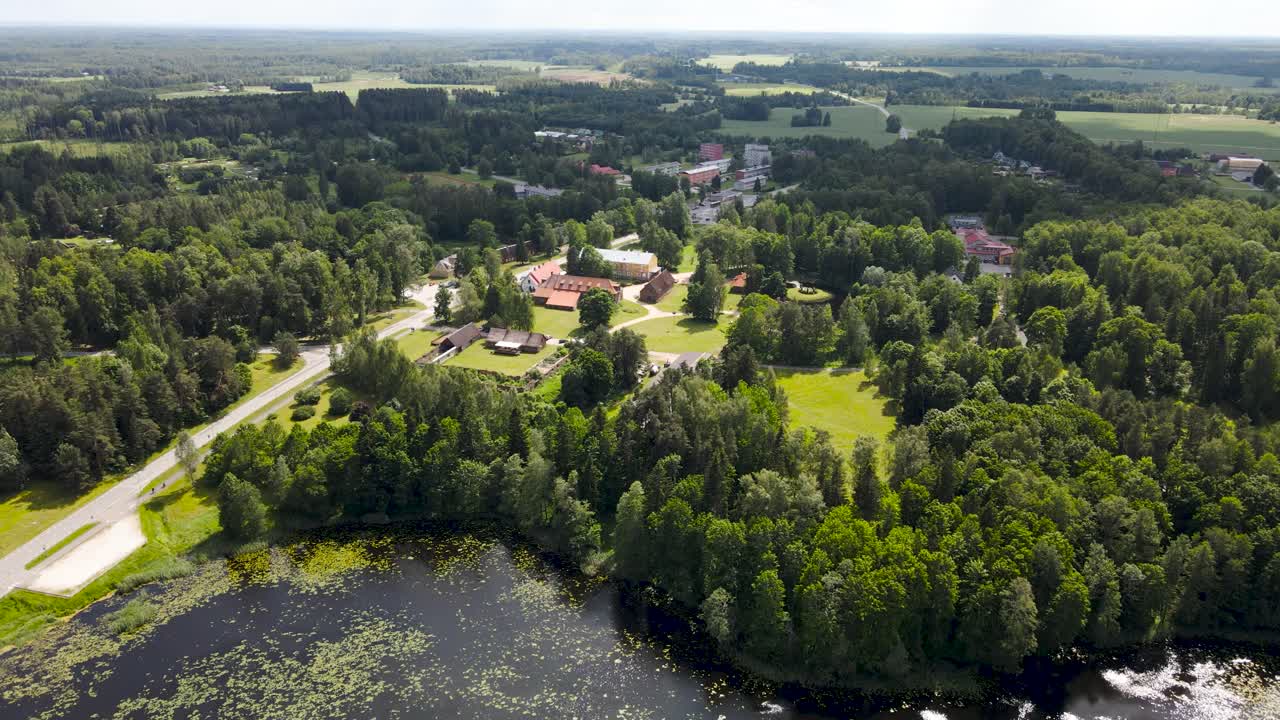 Beautiful aerial panning drone sot of Alatskivi lake, church and white colored old vintage and historic castle during a summer sunny day. A rural countryside highway with vehivles driving on visible