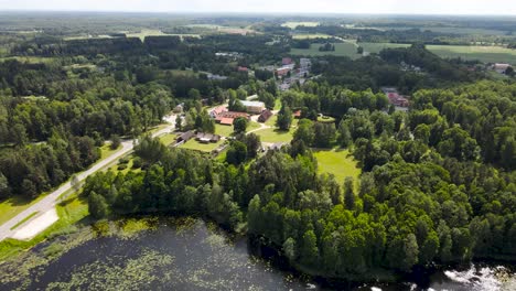 beautiful aerial panning drone sot of alatskivi lake, church and white colored old vintage and historic castle during a summer sunny day. a rural countryside highway with vehivles driving on visible