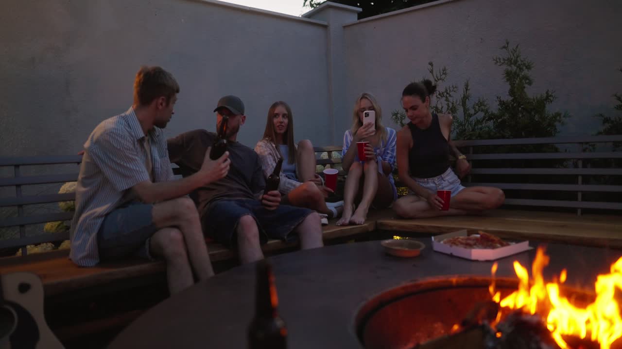 A group of friends are sitting near a fire, chatting and having a happy time while relaxing in the courtyard of a country house