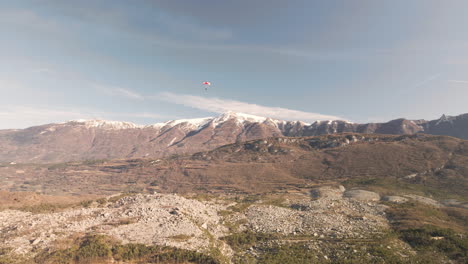 paraglider with snowcapped mountains in background on sunny winter day in trentino, italy