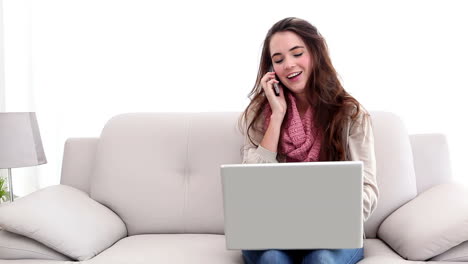 una morena bonita usando una computadora portátil y hablando por teléfono.