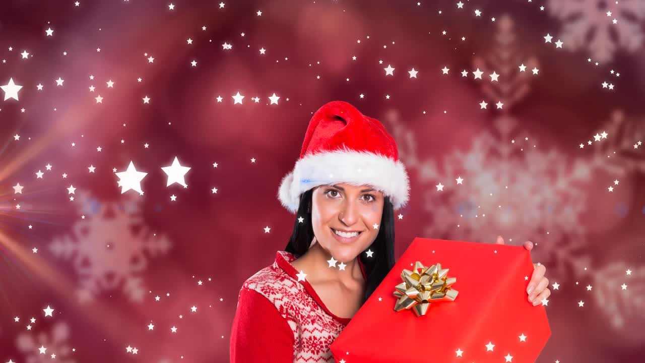 animación de estrellas cayendo sobre feliz mujer caucásica con sombrero de santa manteniendo presente