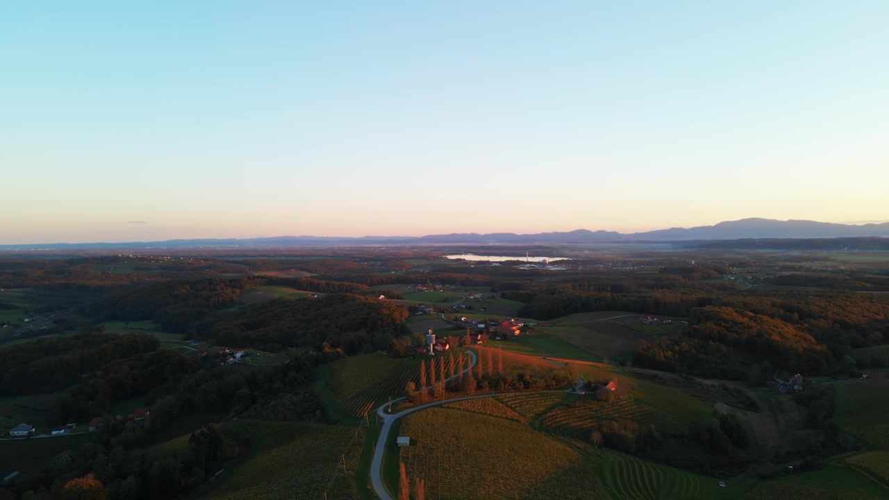 Ampie riprese con drone catturano tranquilli campi agricoli, strade tortuose, case sparse e montagne distanti nella splendida luce dell'ora d'oro.