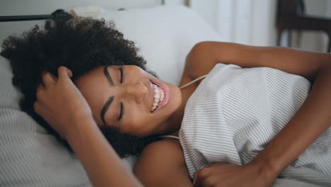retrato de modelo sonriente acostando la cama en casa. mujer de cabello rizado feliz mirando la cámara