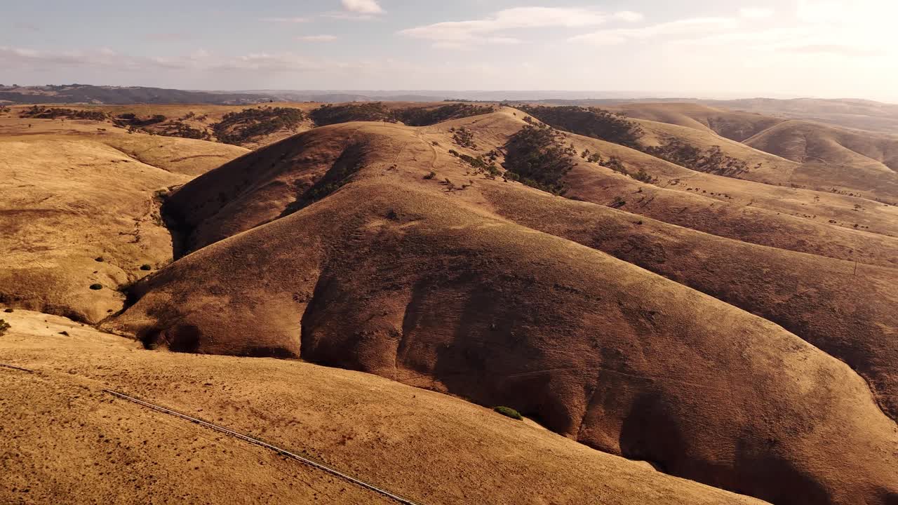 Plano aéreo de presentación con movimiento de cámara de un paisaje costero ondulado y colinas secas cerca de Sellicks Beach, Australia, brillo del mediodía