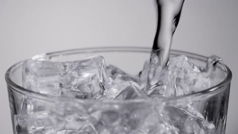 close up slow motion water pouring into glass with ice cubes