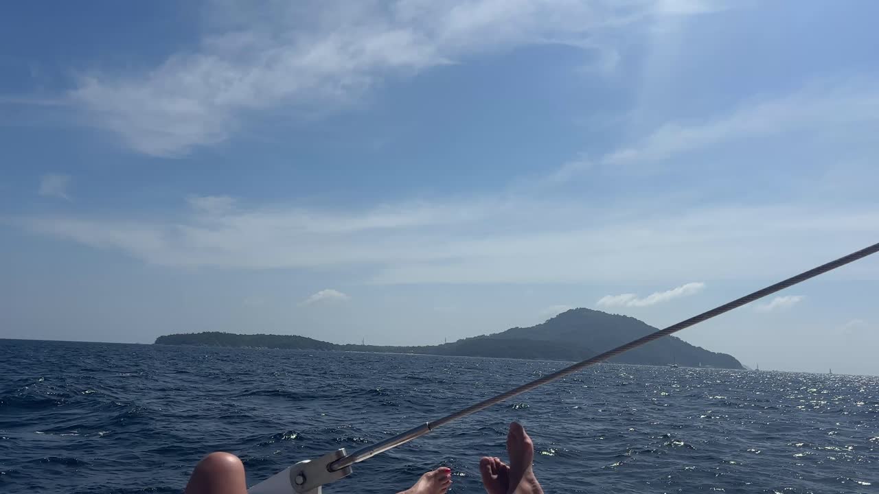 Catamarano che naviga nell'oceano aperto vicino a Phuket con silhouette di isole in lontananza, cielo blu e onde leggere che creano un'atmosfera di viaggio rilassante e un tranquillo paesaggio marino estivo