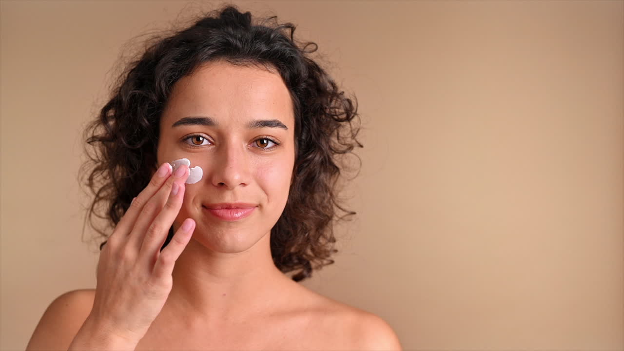 A young caucasian smiling woman is making a face mask, looking into the camera. Slow motion