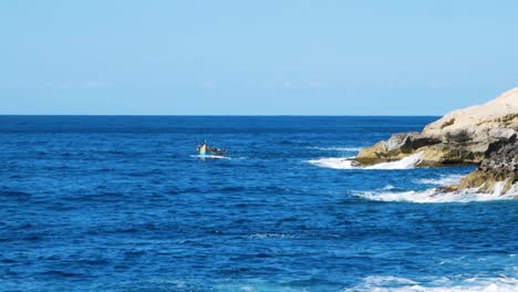 local maltese man sailing near rocky coastline while waves hitting stone