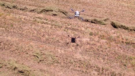 a white agricultural drone flying over the farm fields on a sunny day close to landing moving the grass with the wind it produces, aerial technological equipment