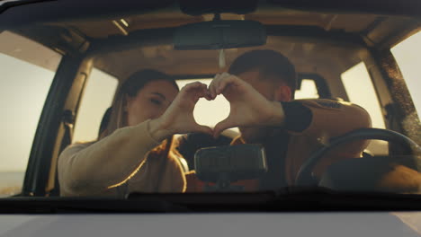 pareja haciendo el símbolo del amor en el coche
