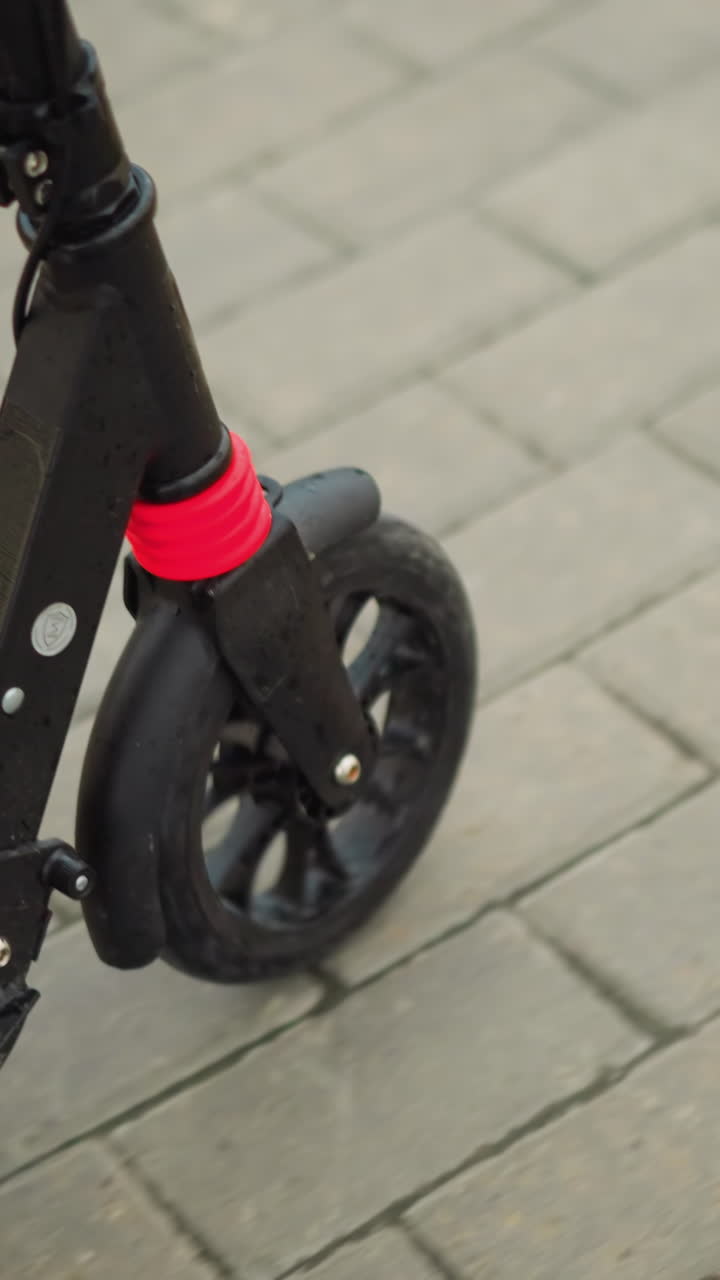 Close-up of a woman's foot with painted nails, wearing white sandals, riding a black scooter on an interlocked pathway