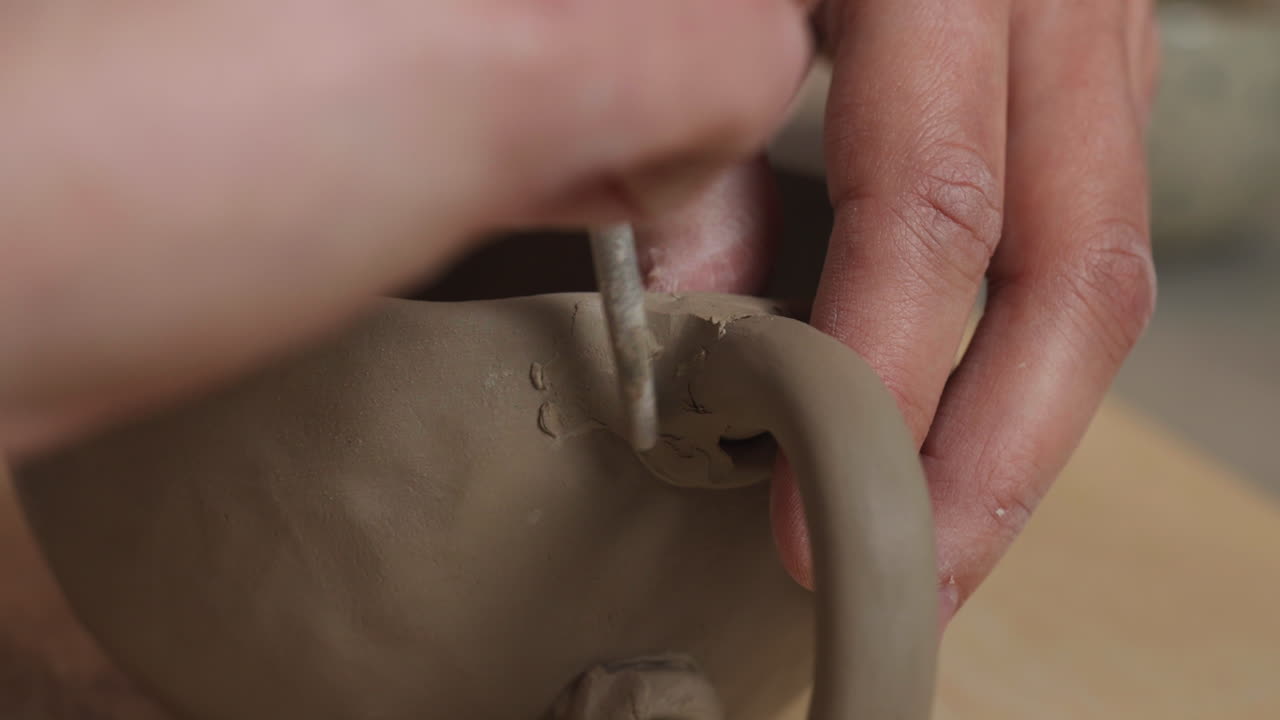 Close up shot of white hands making mug and molding clay with a brush, interior