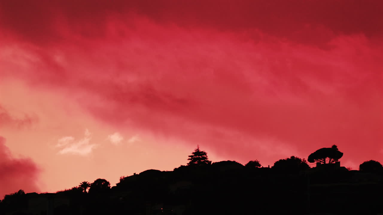 Silhouette di alberi e colline sotto un intenso cielo rosso al tramonto