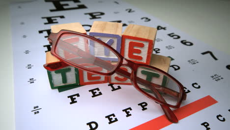gafas que caen sobre la prueba de ojos con bloques de madera deletreando la prueba de ojo