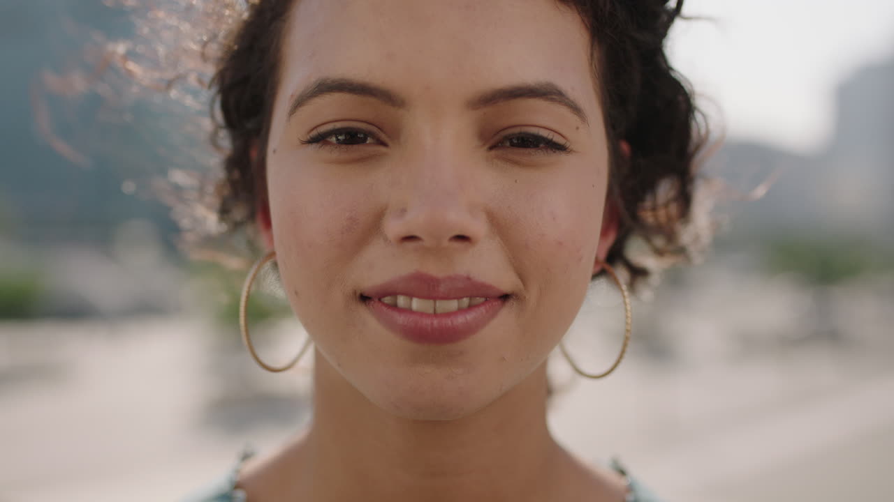 retrato en primer plano de una joven hispana linda que mira sonriendo alegremente a la cámara en el fondo de una ciudad soleada disfrutando del estilo de vida urbano