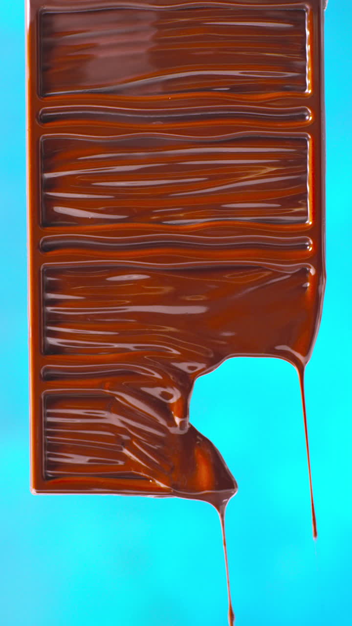 video vertical de primer plano de una barra de chocolate derretida contra un fondo de color azul con espacio de copia 1