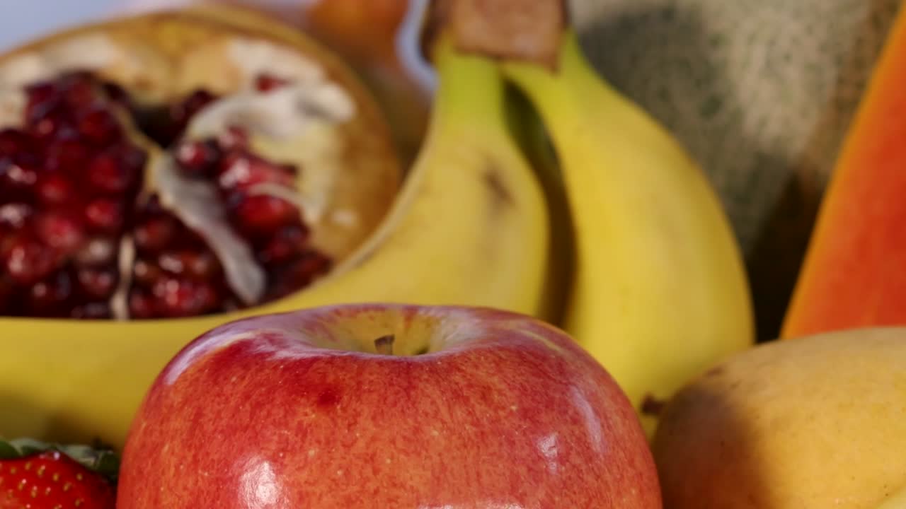 Et fargerikt arrangement med epler, bananer, granatepler, jordbær og cantaloupe i en frisk, levende presentasjon.