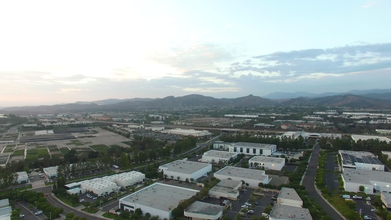 Aerea: Panorami celesti all'ora d'oro in panoramica su città e attività commerciali suburbane nella California meridionale, verso la catena montuosa e i parchi sottostanti.