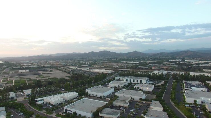 Aerea: Panorami celesti all'ora d'oro in panoramica su città e attività commerciali suburbane nella California meridionale, verso la catena montuosa e i parchi sottostanti.