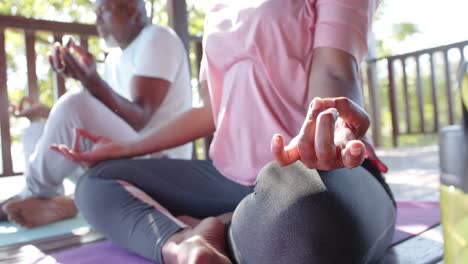 focused senior african american couple practicing yoga meditation on sunny terrace, slow motion