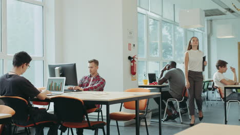 Chica-Seria-Entrando-Al-Espacio-De-Coworking.-Hombres-Jóvenes-Trabajando-En-Espacios-Abiertos.