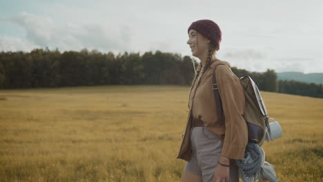 young woman wearing backpack walking by grass