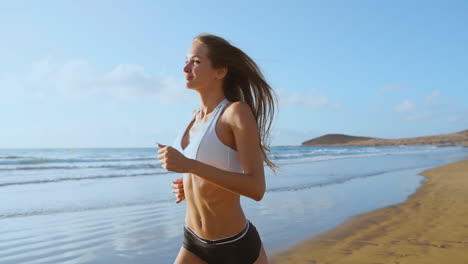 beautiful woman in sports shorts and t-shirt running on the beach with white sand and blue ocean water on the island in slow motion steadicam. waves and sand hills on the back won