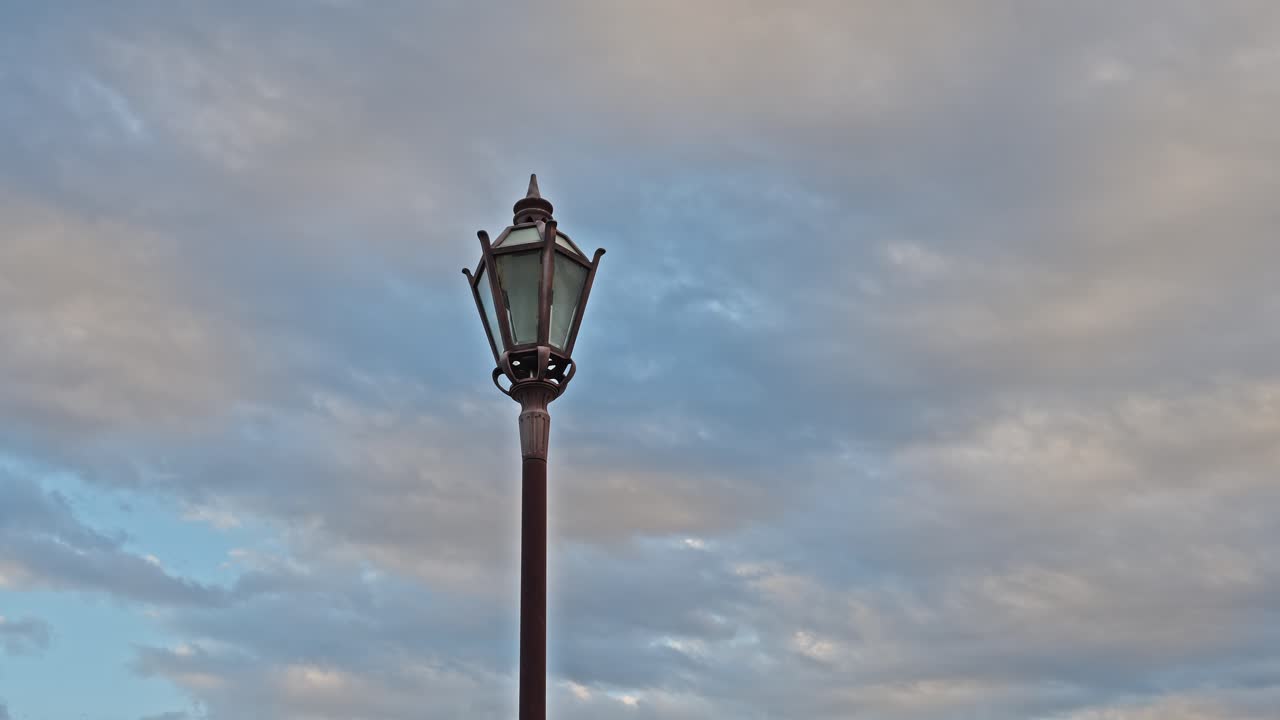 A single ornamental lamppost standing tall against a background of dramatic, fast-moving evening clouds