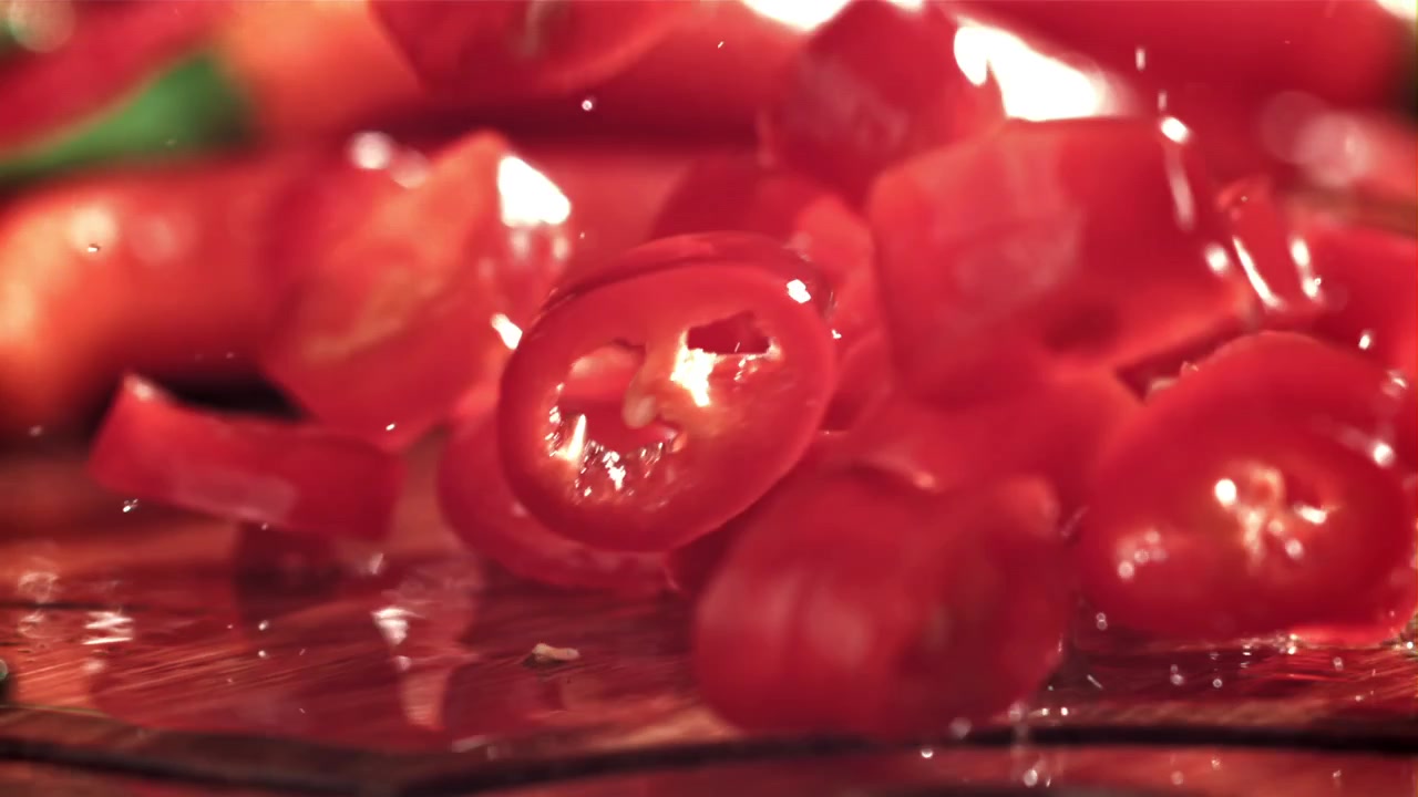 Pedaços de Pimenta Vermelha Caindo e Espirrando em Câmera Lenta sobre Superfície Molhada