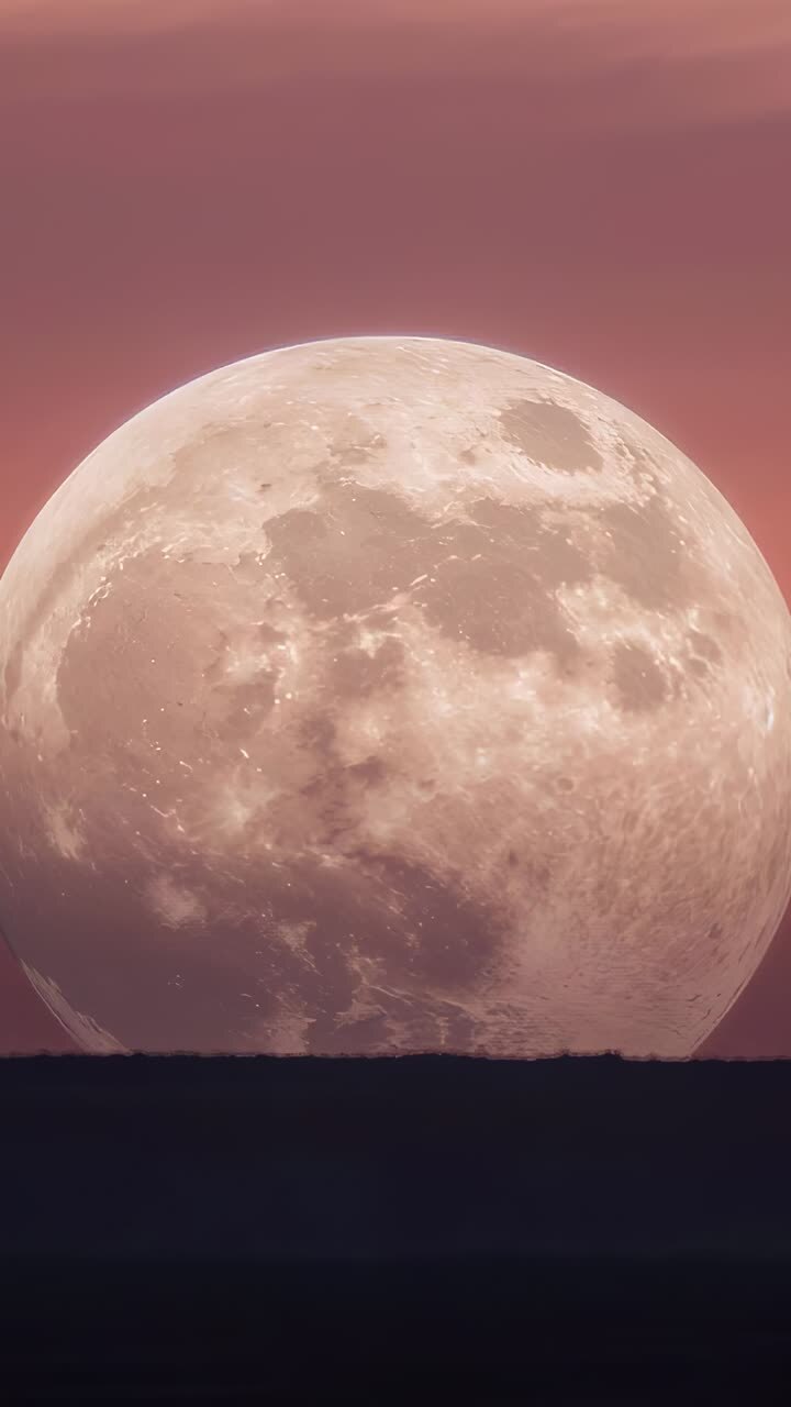 Video im Hochformat: Aufgehender, großer Mond, der sich über einem dunklen Horizont bewegt, während die Dämmerung hereinbricht und Krater sichtbar werden